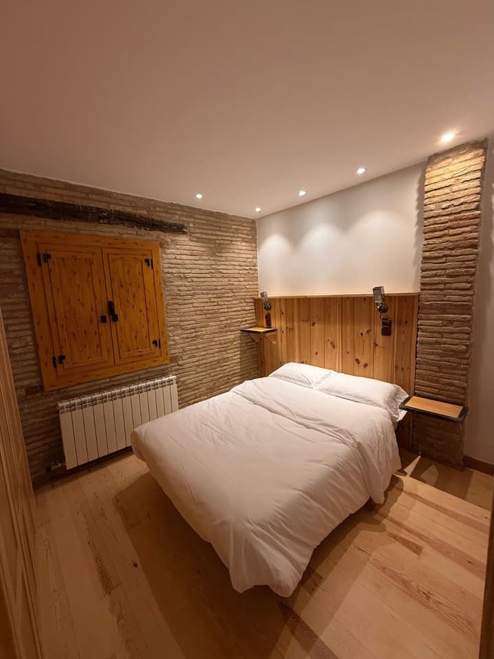 Dormitorio reformado con pared de ladrillo recuperado y contraventana de madera a medida