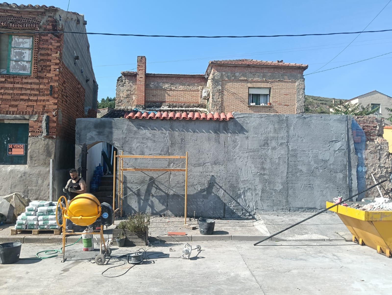 Muro de fachada en plena obra, enfoscado en gris con el remate de teja recién colocado
